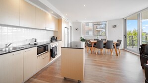 Une cuisine moderne avec des meubles en bois, un plan de travail noir et un îlot central. On y trouve un coin repas avec une table et des chaises, ainsi qu’une grande fenêtre donnant sur l’extérieur.