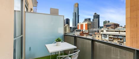 A balcony with a small table and chair, a potted plant, and a cityscape view.