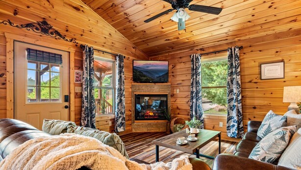 A cozy cabin interior with a fireplace, leather furniture, and a ceiling fan. - Pinot Paradise (Pigeon Forge)