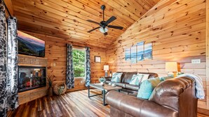 A cozy cabin interior with a wooden ceiling, a fireplace, a leather sofa, and a television. - Pinot Paradise (Pigeon Forge)