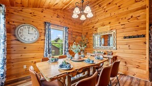 A wooden interior with a dining table set for four, a clock, and a mirror. - Pinot Paradise (Pigeon Forge)