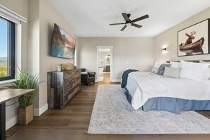A bedroom with a bed, a ceiling fan, a painting, and a view through a window.
