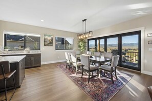 A dining area with a large table and chairs, a kitchen with dark cabinets, and a view of the mountains through large windows.