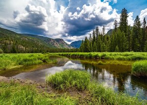 A serene river with lush greenery and tall trees, surrounded by mountains under a partly cloudy sky. - New built, stunning home with Hot Tub, 5/4, near Granby Ranch - sleeps 16 (Granby)