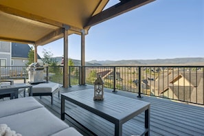 En overdækket terrasse med udsigt over et boligområde, grill og en lygt.