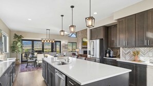 A modern kitchen with a large island, dark cabinets, and pendant lighting. - New built, stunning home with Hot Tub, 5/4, near Granby Ranch - sleeps 16 (Granby)