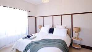 A bedroom with a bed, bedside tables, a chandelier, and a window with curtains. - Heritage Home With BBQ & Outdoor Fire Pit (Tenterfield)