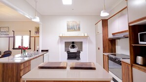 A modern kitchen with a central island, wooden cabinets, a microwave, stove, and a painting above the fireplace. - Heritage Home With BBQ & Outdoor Fire Pit (Tenterfield)