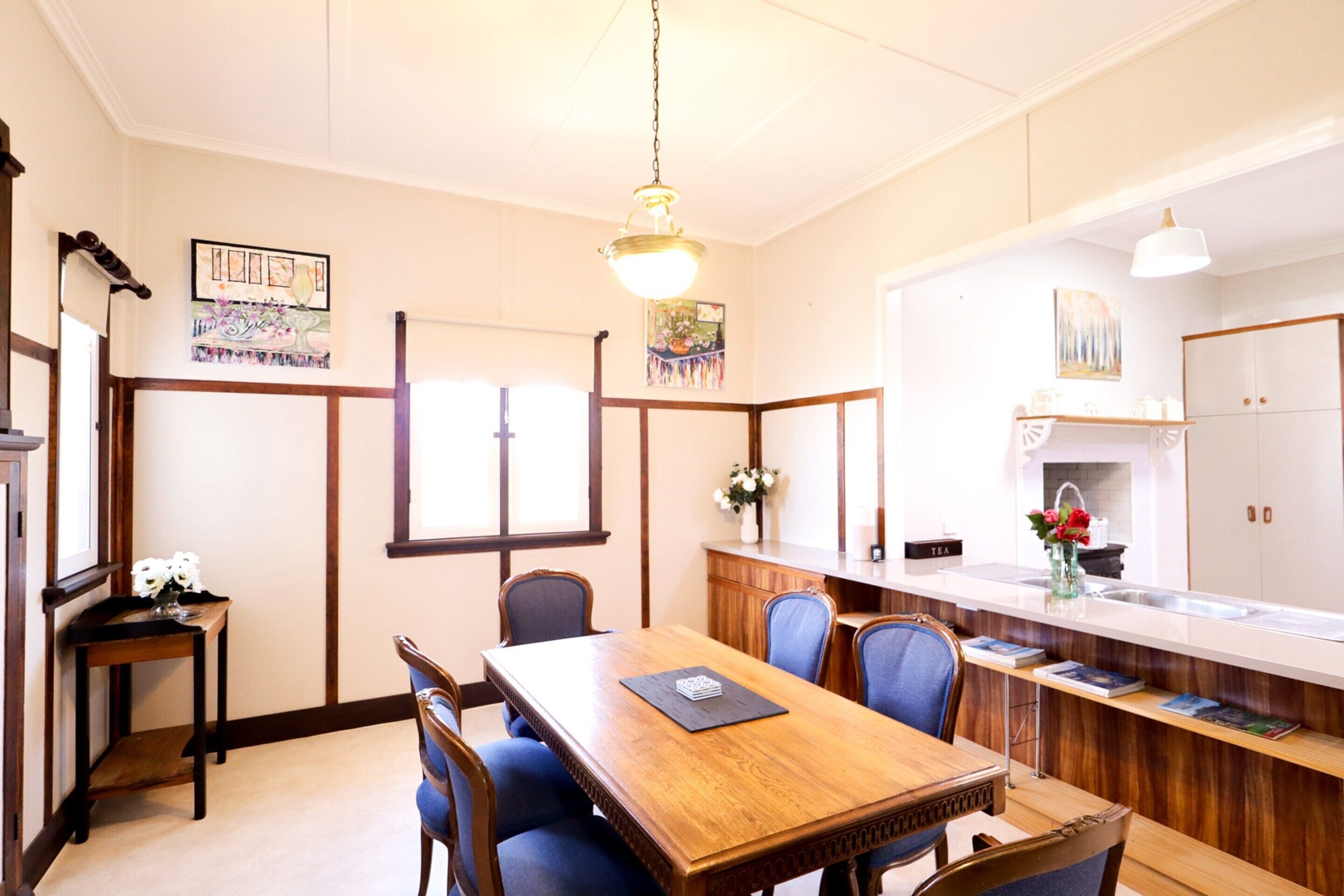 Un comedor con mesa y sillas de madera, una cocina con pileta y alacenas, y obras de arte en las paredes.