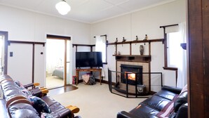 A living room with a fireplace, leather sofas, a television, and a wooden ceiling. - Heritage Home With BBQ & Outdoor Fire Pit (Tenterfield)