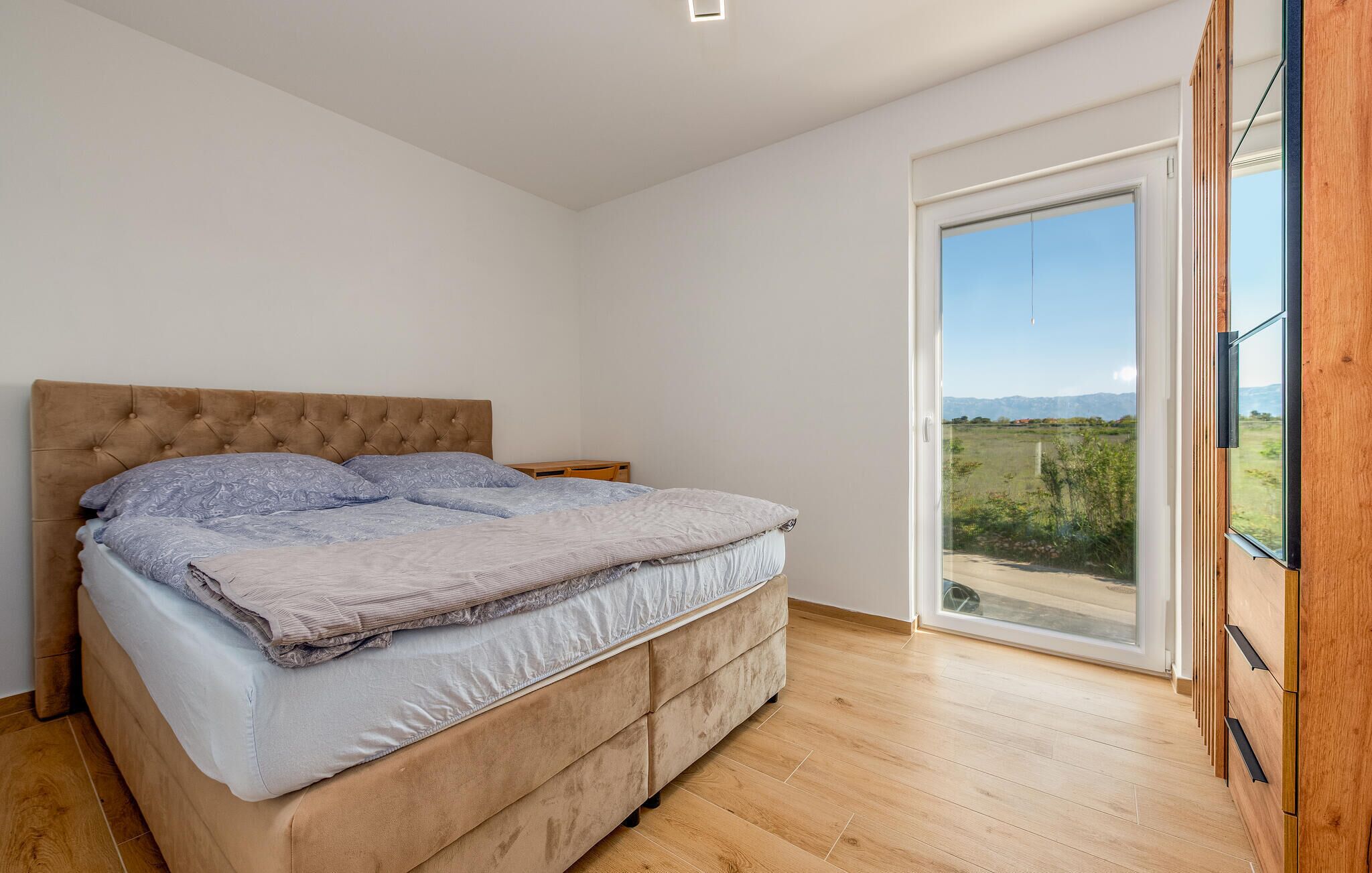 Une chambre avec un grand lit, un plancher en bois, une fenêtre donnant sur un beau paysage et un luminaire au plafond.