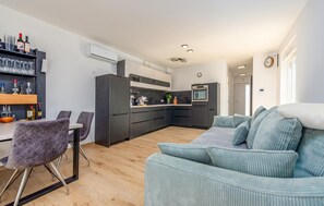 Una cocina moderna con armarios oscuros, una zona de comedor con mesa y sillas, y una sala de estar con sofá.