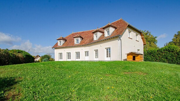 Ein zweistöckiges Haus mit einem geneigten Dach, zahlreichen Fenstern und einem kleinen Anbau.
