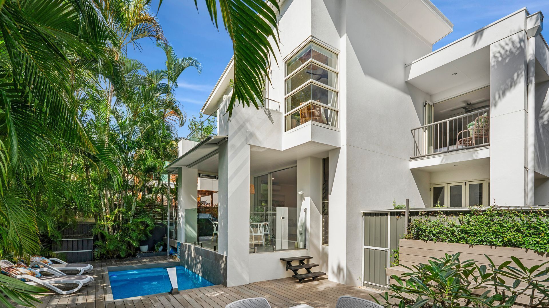A modern two-story house with a swimming pool, outdoor seating, and lush greenery.