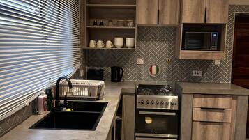 Una cocina moderna con estufa, horno y microondas integrados. Cuenta con gabinetes de madera y un elegante salpicadero con patrón de espiga.