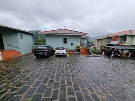 Um caminho de paralelepípedos leva a um edifício com telhado de telhas vermelhas, carros estacionados e uma escadaria.