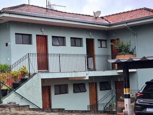 A two-story building with a balcony, a satellite dish, and a car parked in front. - Lindo loft decorado centro com garagem (São Roque)