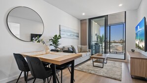 A modern living room with a dining area, a sofa, a coffee table, and a large window offering a view of the outdoors. - Charming 1-bed With Rooftop Access & Parking (Perth)
