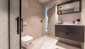 Un baño con inodoro, tocador con espejo y puerta que da a otra habitación.