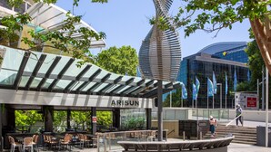 An outdoor café with tables and chairs, a covered seating area, and a distinctive spiral sculpture in the background.