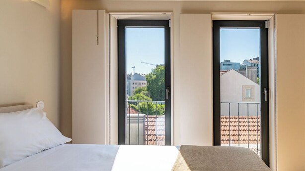 A hotel room with a bed, a window, and a balcony with a view of buildings and trees. - Studio in the center of Porto for tourism or remote work (Porto)