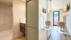 A modern hotel room with a sliding glass door leading to a balcony, a large mirror, a flat-screen TV, and wicker furniture. - Studio in the center of Porto for tourism or remote work (Porto)