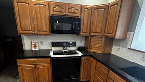 Una cocina con armarios de madera, un microondas negro, una estufa y una encimera negra.