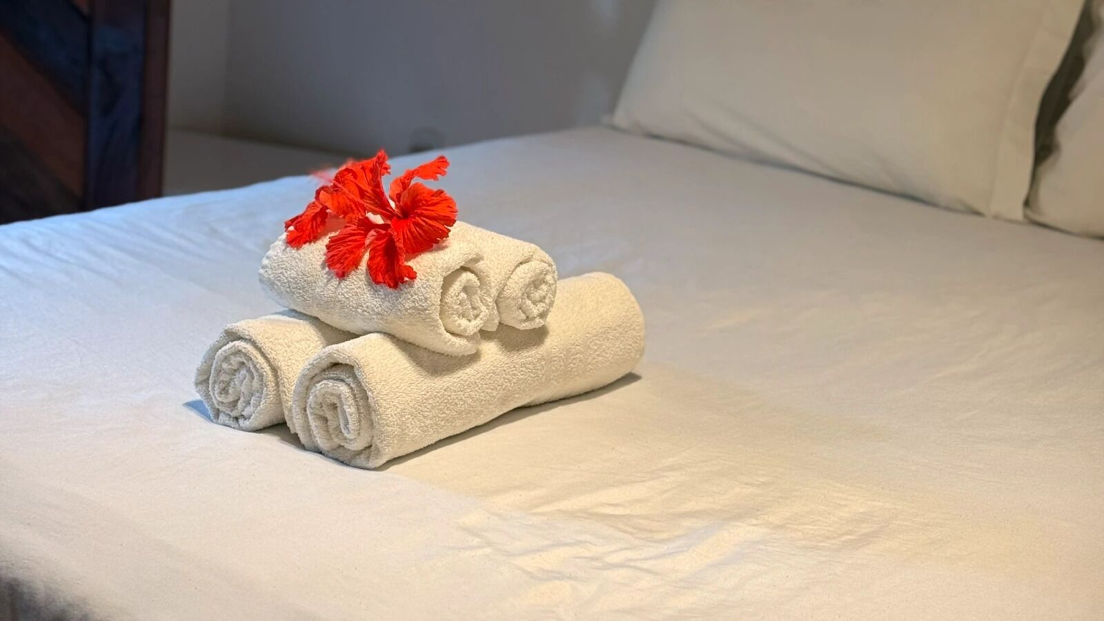 A neatly made bed with white linens and a red flower on top.