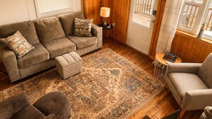 A cozy living room with a sofa, ottoman, and armchair, a patterned rug, a clock, and a door with a balcony view. - Bishop's Landing (Portugal Cove-St. Philip's)