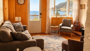 A cozy living room with a wooden ceiling, a sofa, a chair, a small table, and a view of the sea. - Bishop's Landing (Portugal Cove-St. Philip's)
