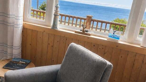 A room with a grey armchair, a wooden window sill, and a view of the ocean. - Bishop's Landing (Portugal Cove-St. Philip's)