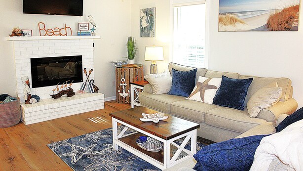 A living room with a white fireplace, a beige sofa with blue cushions, a wooden coffee table, and a blue rug. - Time to relax and enjoy (New Bern)