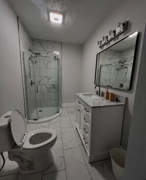 A bathroom with a toilet, a shower with a glass door, a sink with a marble countertop, and a mirror above the sink. - Impeccable 3BR Home Mins to IU Health & Downtown (Indianapolis)