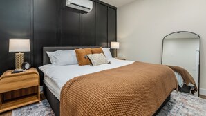 A modern bedroom with a dark wood headboard, a large bed with a brown knitted blanket, two bedside tables with lamps, and a large mirror on the wall. - Stylish 1BR Downtown • Near Garden of the Gods (Harrisburg)