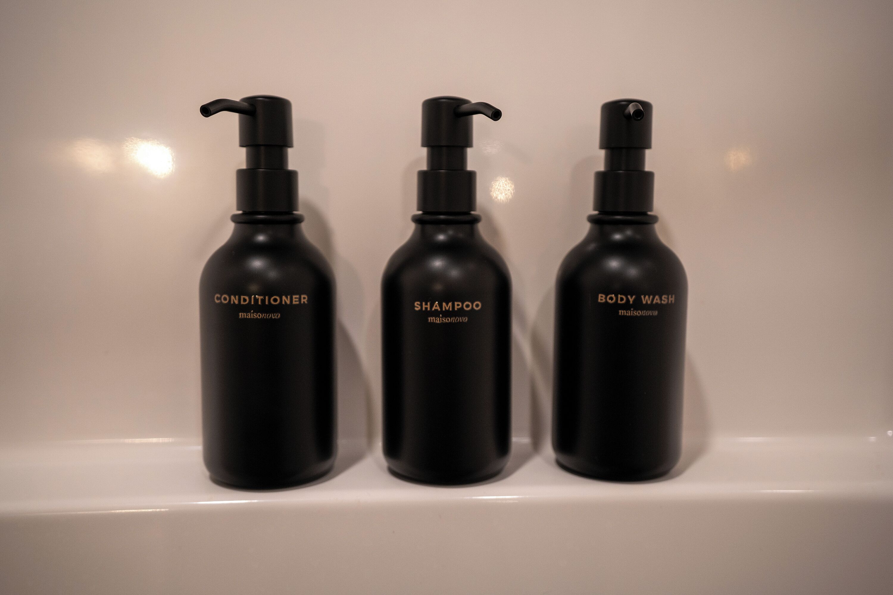 Trois flacons noirs de produits de toilette sont posés sur une étagère blanche.