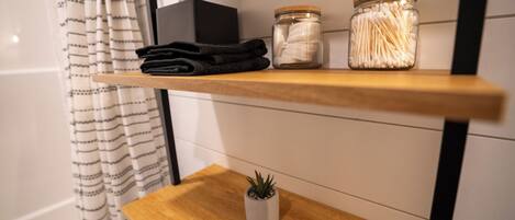 Une étagère avec une serviette pliée, deux pots de cotons-tiges et une petite plante en pot.