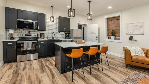 A modern kitchen with dark cabinets, a central island with bar stools, a coffee machine, and a refrigerator. - Stylish 1BR Downtown • Near Garden of the Gods (Harrisburg)