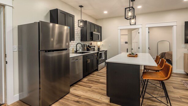 Una cocina moderna con electrodomésticos de acero inoxidable, armarios negros y una isla central con taburetes de bar.