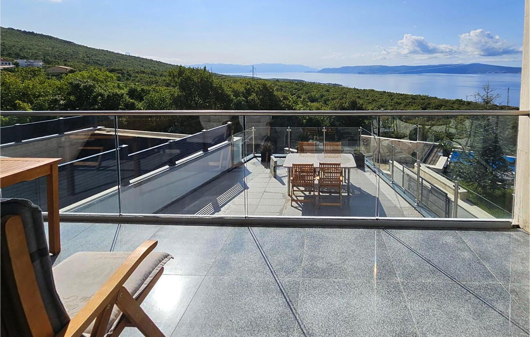 A glass-enclosed terrace with a table and chairs, offering a view of a lake and distant mountains.