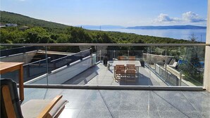A glass-enclosed terrace with a table and chairs, offering a view of a lake and distant mountains.