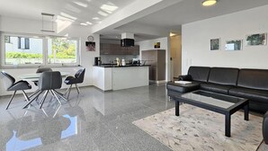 A modern living room with a black leather sofa, a glass coffee table, and a dining area with a white table and black chairs.