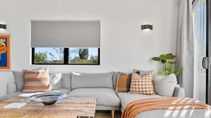 Ein modernes Wohnzimmer mit einer Couch, einem Couchtisch und einem großen Fenster mit Blick auf Bäume.