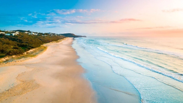 Ein Strand mit blauem Himmel, sandigem Ufer und einer fernen Küstenlinie mit Gebäuden.