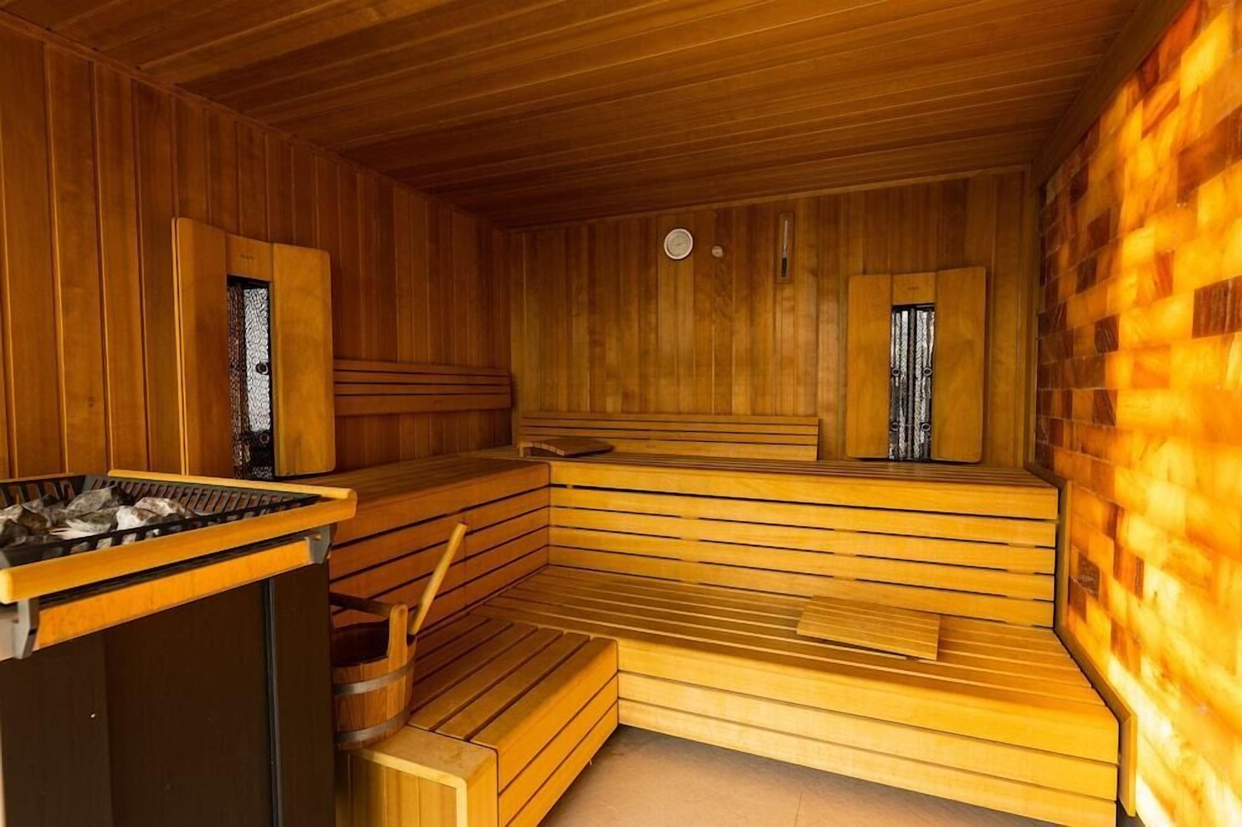 A sauna with wooden benches and a bench seat, a heater, and a small table.