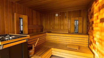 Un sauna avec des bancs en bois et une banquette, un appareil de chauffage et une petite table.