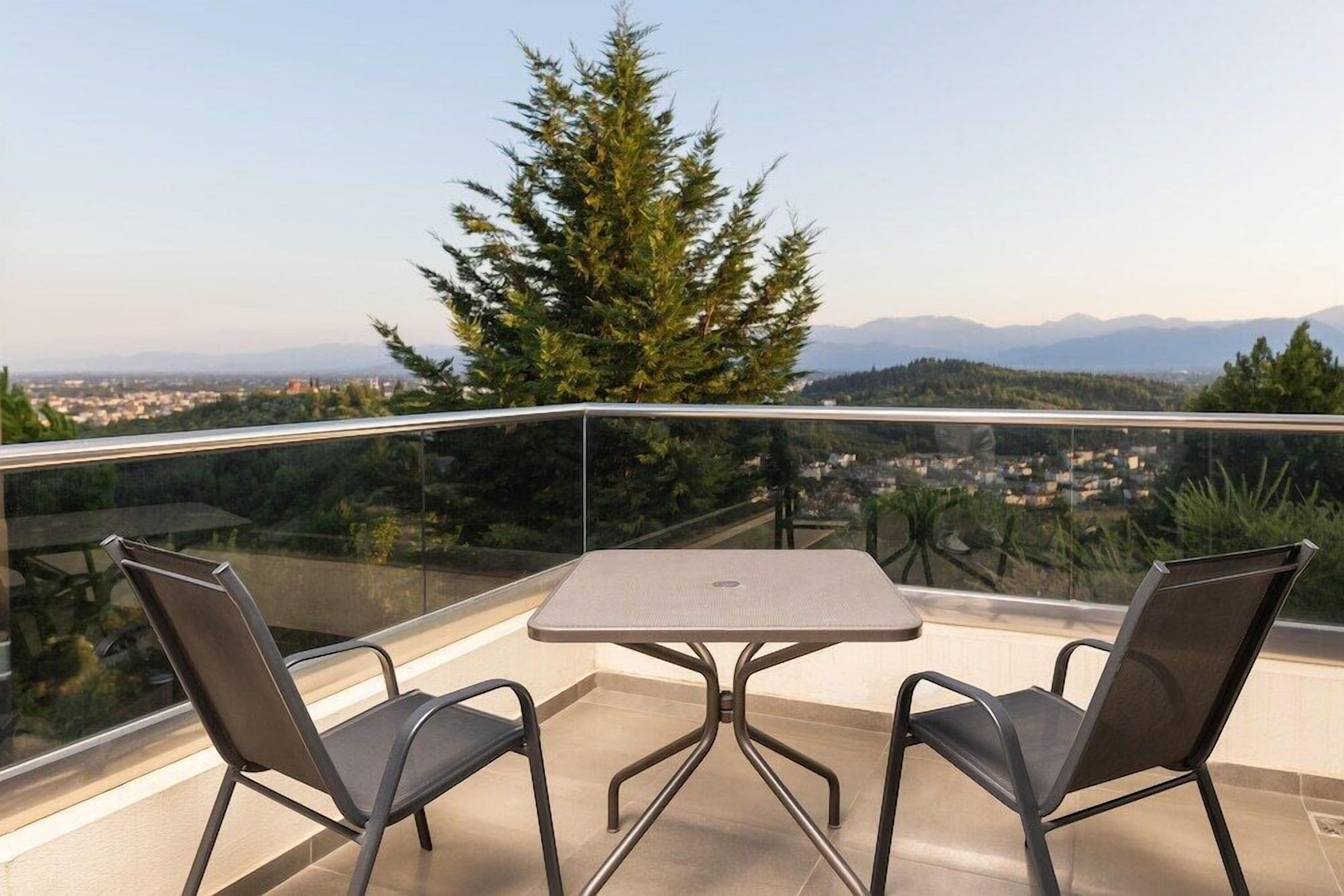 Ein Balkon mit Tisch und zwei Stühlen, mit Blick auf eine Stadtlandschaft und Berge.