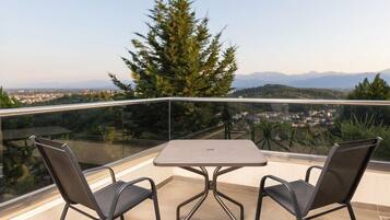 A balcony with a table and two chairs, overlooking a cityscape and mountains.