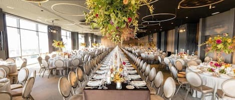 A banquet hall with round tables, chairs, and floral centerpieces.
