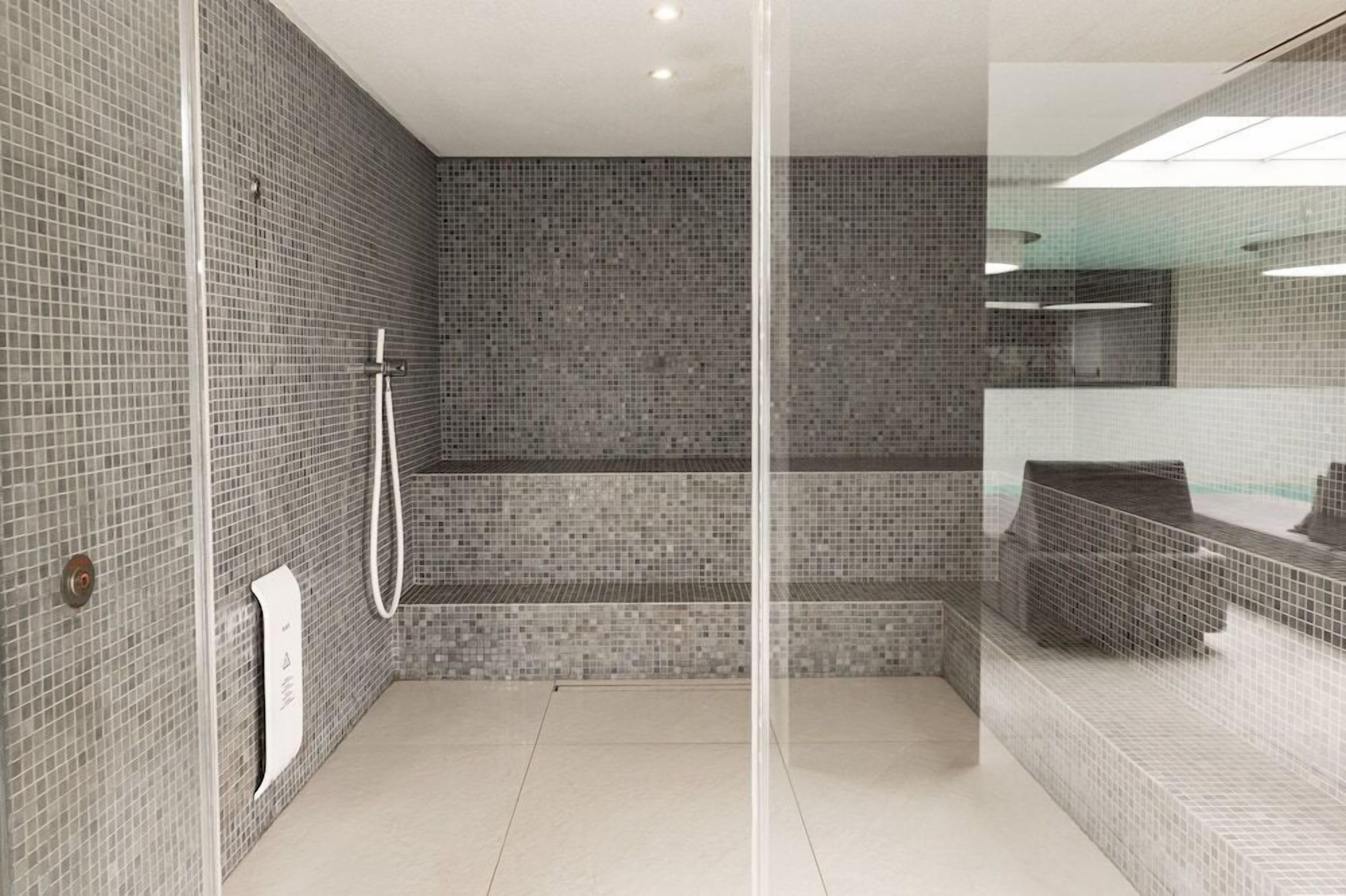 Un baño moderno con cabina de ducha de vidrio, paredes con azulejos y una zona de lavabo a la vista.
