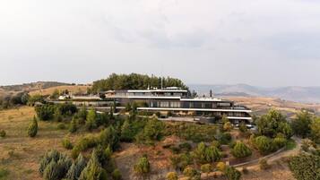 A modern multi-story building with a flat roof, surrounded by a landscaped garden with various shrubs and trees.